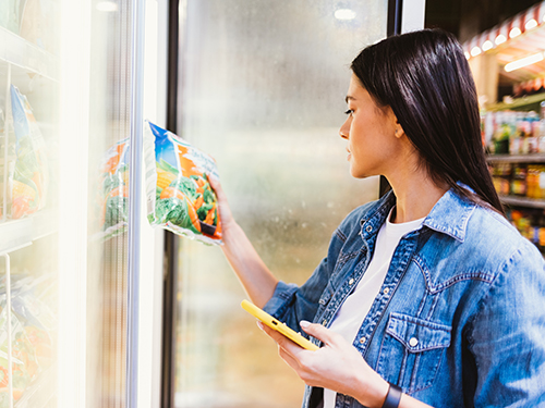 Photo: A smiling man and woman stand in a grocery store aisle, reviewing the label on a packaged food product while holding canned and bottled items.