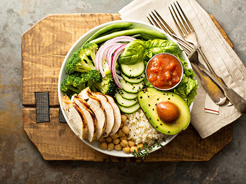 A plate filled with cooked salmon, noodles, broccoli, and slices of apples and oranges.