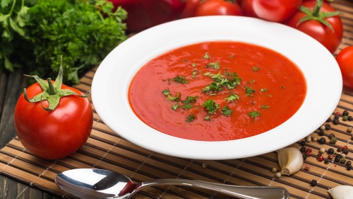 A bowl of tomato soup with fresh tomatoes, garlic, and parsley.