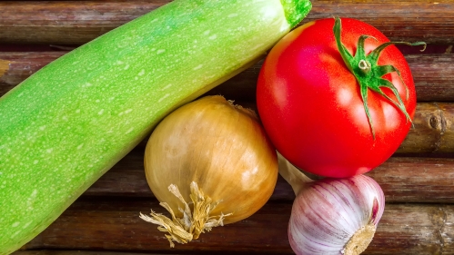 Zucchini, onion, tomato, and garlic on a cutting board.