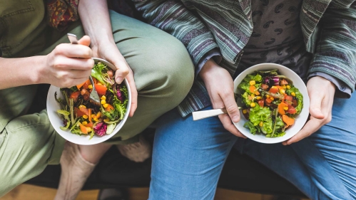 Couple eating healthy salad at home on the sofa.