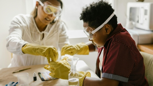 An adult and a child wearing gloves and goggles working on a science experiment.