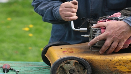 A gentleman utilizes a lug wrench to fix a yellow lawnmower that seems to have had plenty of use.