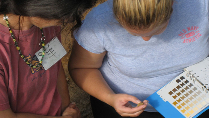 Two people holding a binder with color swatches learning to distinguish the nuances of soil color are seen from above.