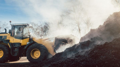 A bulldozer pushes compost and dirt into a large pile. Steam is coming off of the pile.
