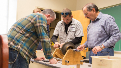 People standing in a classroom around a desk examining how a pump device works.