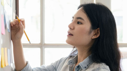 Woman holding a pencil stands in front of a whiteboard covered in post-it notes