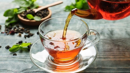 Pouring black tea into glass cup on wooden table 