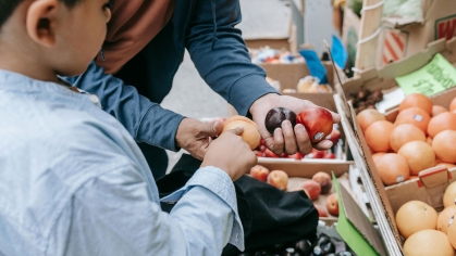 An adult and a child buying fruit at a market.