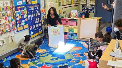 A teacher and several children sitting in a circle on a rug in a classroom.