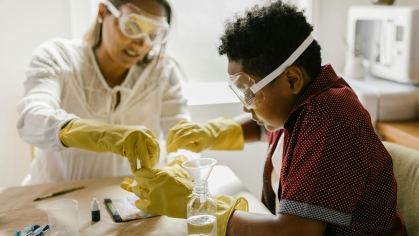 An adult and a child wearing gloves and goggles working on a science experiment.