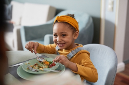 African-American girl eating food at table and smiling happily